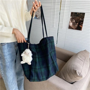 Detail of green plaid wool tote bag featuring a cute white plush lamb pendant accessory