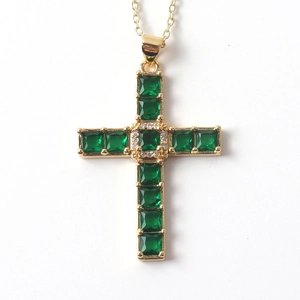 Detailed close-up of golden cross necklace with green gemstones and zircon accents