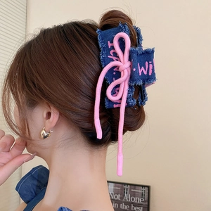 Detail of blue denim claw clip with pink rope bow on model's hair, side-back view