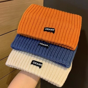 Close-up of three knitted beanies in orange, blue and beige with GRANK woven labels