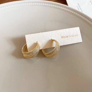 Detailed macro view of gold-plated multi-layered C-shaped earrings with woven texture