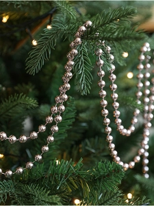 Close-up of silver Christmas bead chain wrapped around pine branches with festive lights