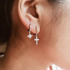 Detailed view of silver hoop earrings featuring a sparkling cross and star pendant