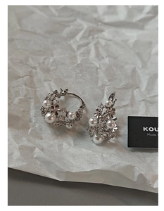 Close-up of asymmetric hollow pearl earrings with zircon inlay on wrinkled paper