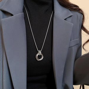 Detail of silver multi-layer circle pendant necklace worn over a black turtleneck sweater