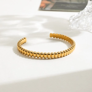 Détail d'un bracelet jonc doré minimaliste avec texture verticale et éclat poli