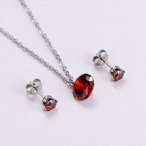 Detail of silver necklace and earrings set with round faceted red gemstones on white background