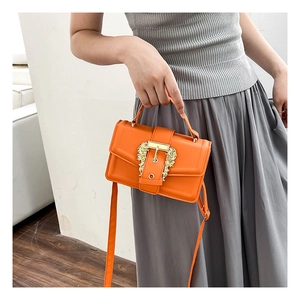 Detail of bright orange crossbody bag with ornate gold baroque buckle and top handle