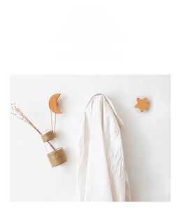 Detail of moon and star wooden wall hooks holding a vase and white shirt on a wall