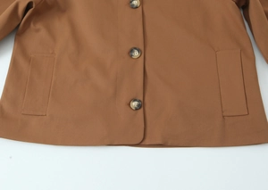 Detail of brown short trench jacket showing amber resin buttons and side pockets texture