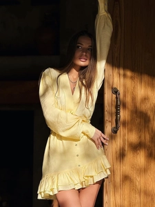 Close-up of a pale yellow V-neck dress featuring button details and ruffled hem design