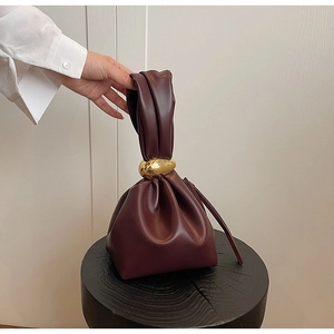 Close-up of pleated dark burgundy handbag with large golden spherical metal hardware details