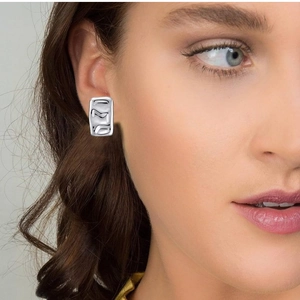 Close-up of silver rectangular earring with irregular wavy texture on female model
