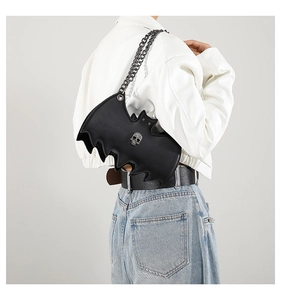 Detail of bat-shaped crossbody bag with metal chain strap and skull ornament on model