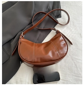 Brown faux leather crescent bag with adjustable strap next to a smartphone for size reference
