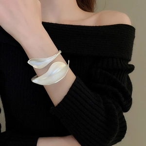 Close-up of a silver leaf-shaped open cuff bracelet worn over a black sweater sleeve