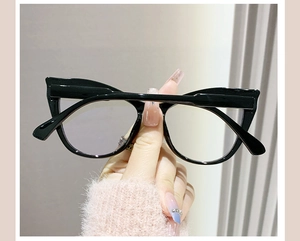 Detail shot of cat-eye black frames with clear lenses held by a model in pink