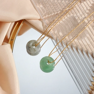 Detail of round malachite and agate stone pendants on gold chains over silk fabric