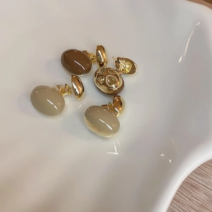 Détail de boucles d'oreilles ovales en résine café et beige sur plateau en céramique doré