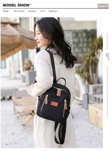 Outdoor shot of a compact black nylon backpack with gold zippers worn by a model