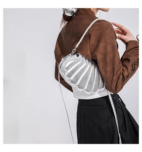 Detail einer silbernen muschelförmigen Umhängetasche mit Perlenkette am Modell