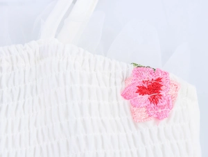 Détail d'une robe blanche froncée avec broderie fleur rose et bretelle en tulle