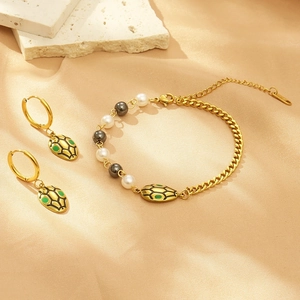 Detailed shot of gold snake-pattern earrings and faux pearl bracelet on stone background