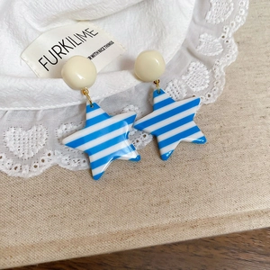 Close-up of blue and white striped star-shaped resin drop earrings on lace