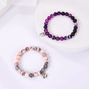 Close-up of purple agate and zebra stone bracelets with apple pendants on white stands