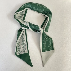 Detailed close-up of a green floral silk twilly scarf tied neatly on a plain white background