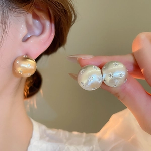 Close-up of matte champagne gold spherical stud earrings with embossed star texture