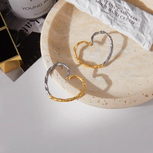 Close-up of textured heart earrings in mixed metal tones on a marble tray