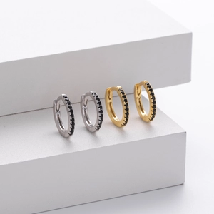 Macro detail of silver and gold huggie earrings featuring rows of small black zircon stones