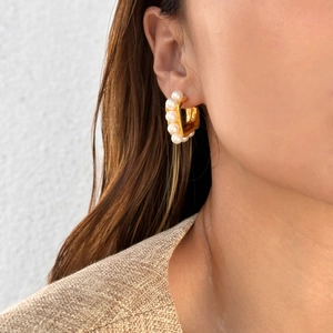 Detail of elegant gold hoop earrings with white pearls on a model wearing a knit sweater