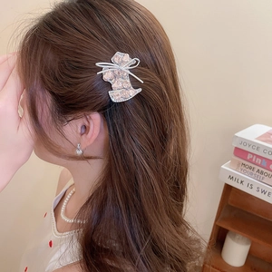 Detail showing a bow-shaped hair clip with pink crystals on a model with pearls
