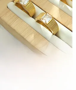 Close-up of gold ring with pleated texture and square crystal stone on a stand
