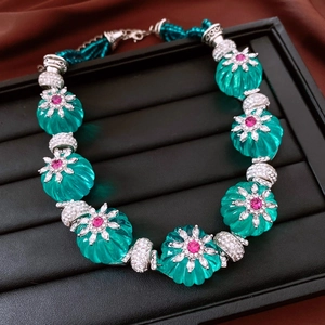Détail de perles facettées vert émeraude et collier floral argenté sur plateau de bijoux