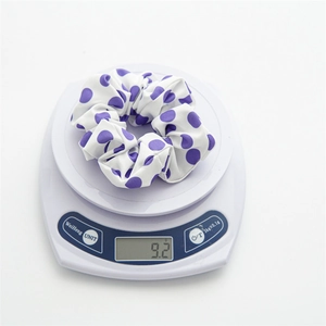 Polka dot hair scrunchie in purple and white being weighed on a digital scale showing 9.2g