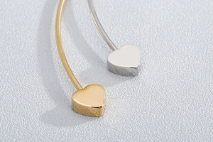 Close-up of minimalist gold and silver heart-shaped stud earrings in polished stainless steel