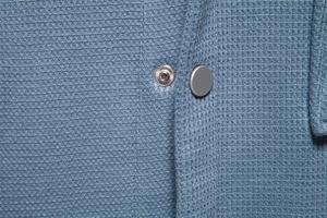 Macro shot of blue waffle texture fabric and matte grey snap button on a men cardigan