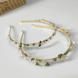 Detail of elegant gold headband with white pearls, green leaves, and clear crystals