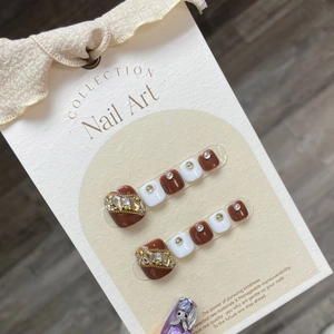 Brown and white press-on toenails with rhinestone and chain accents on beige card