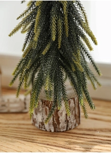 Close-up of a mini Christmas tree with snow-dusted needles on a natural wood base