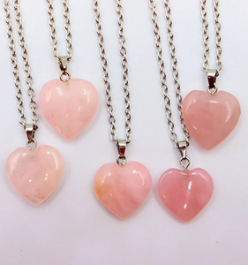 Group of natural rose quartz heart pendants on elegant silver chains on white background