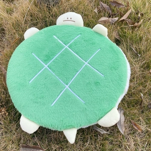 Top view of a plush green turtle-shaped seat cushion with soft fabric on grass
