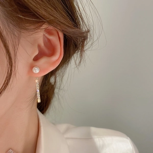 Close-up of pearl stud earring with dangling rhinestone fringe chain on a model