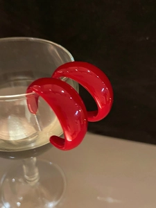 Détail de boucles d'oreilles créoles C rouges en acrylique sur un verre au fini brillant