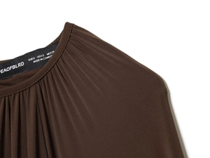 Detail of loose brown crewneck top showing pleated hem and premium silky fabric texture