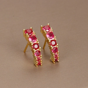 Detail of gold curved earrings featuring multiple red gemstones on a textured surface
