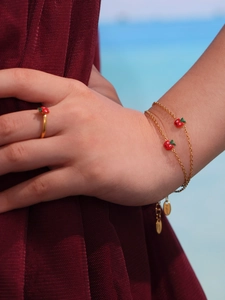 Dettaglio dell'anello con mela rossa e set bracciale dorato su modella in spiaggia